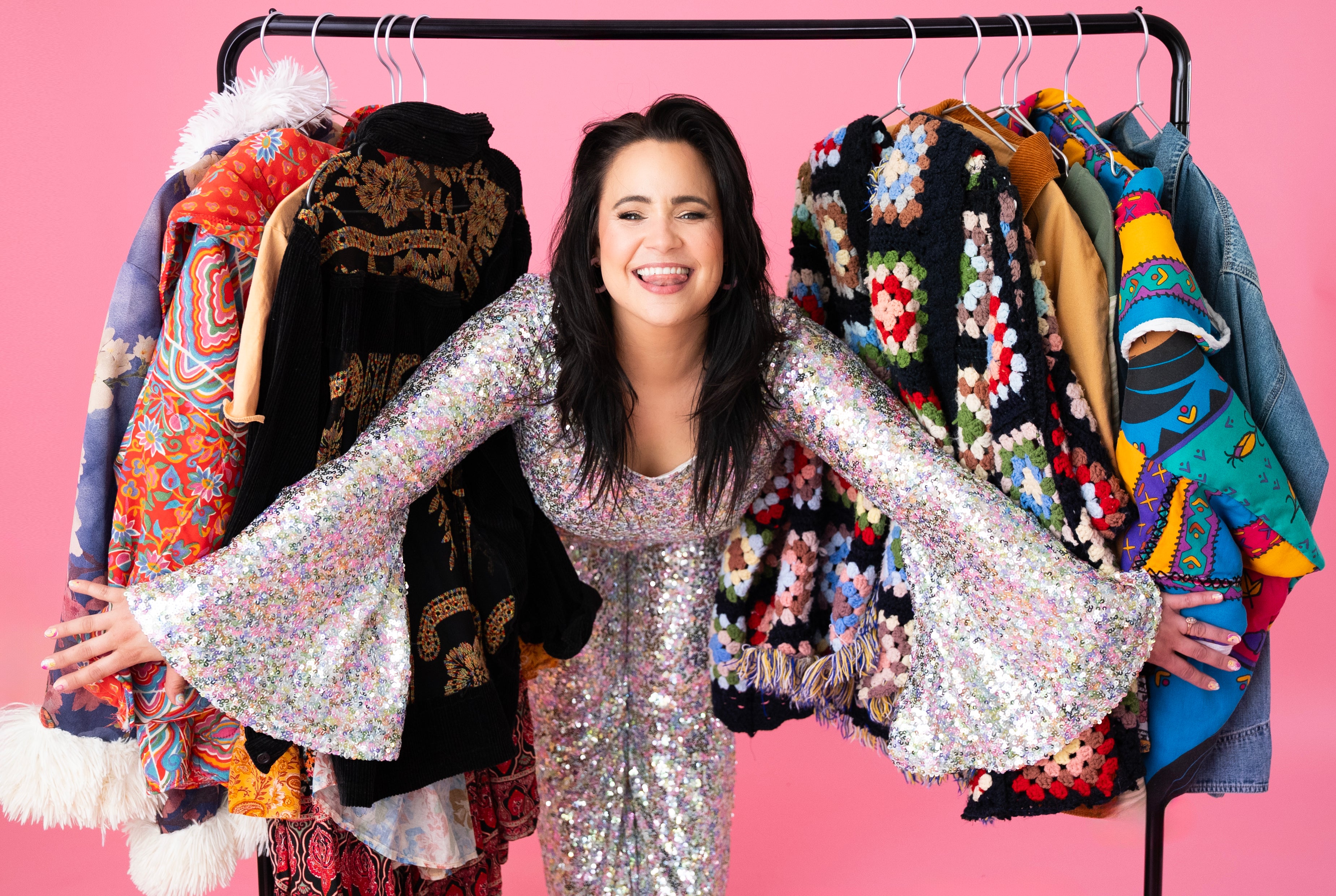 Woman in a silver sequin dress surrounded by colorful clothes on a pink background